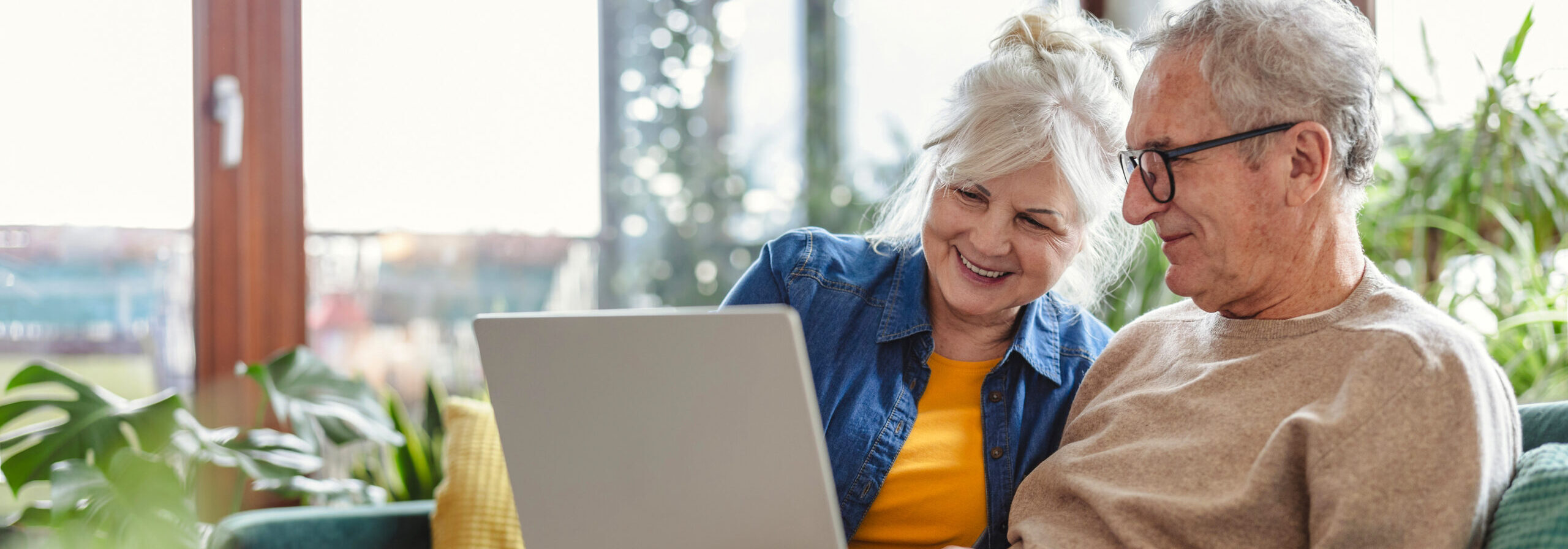 Älteres Ehepaar sitzt mit Laptop am Sofa